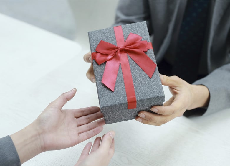 une personnes qui offre un cadeau avec un ruban rouge à une autre personne
